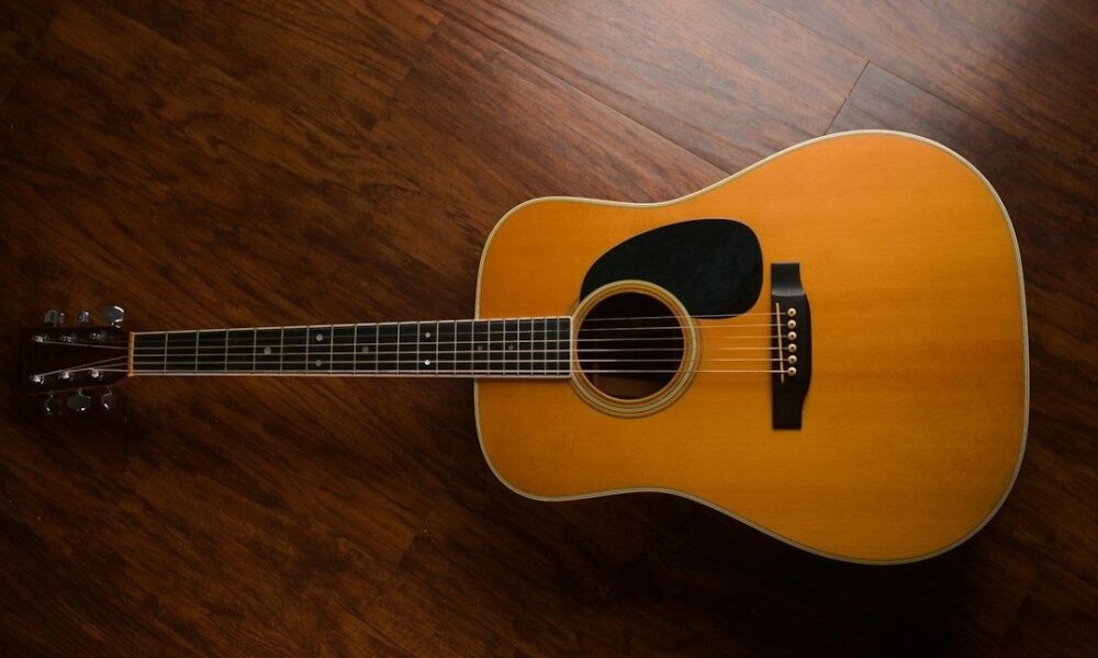Vintage akoestische gitaar met warme houtkleur op een donkere houten vloer